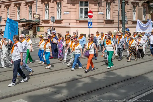 Grupa ludzi w kolorowych strojach maszeruje ulicą, trzymając transparenty.