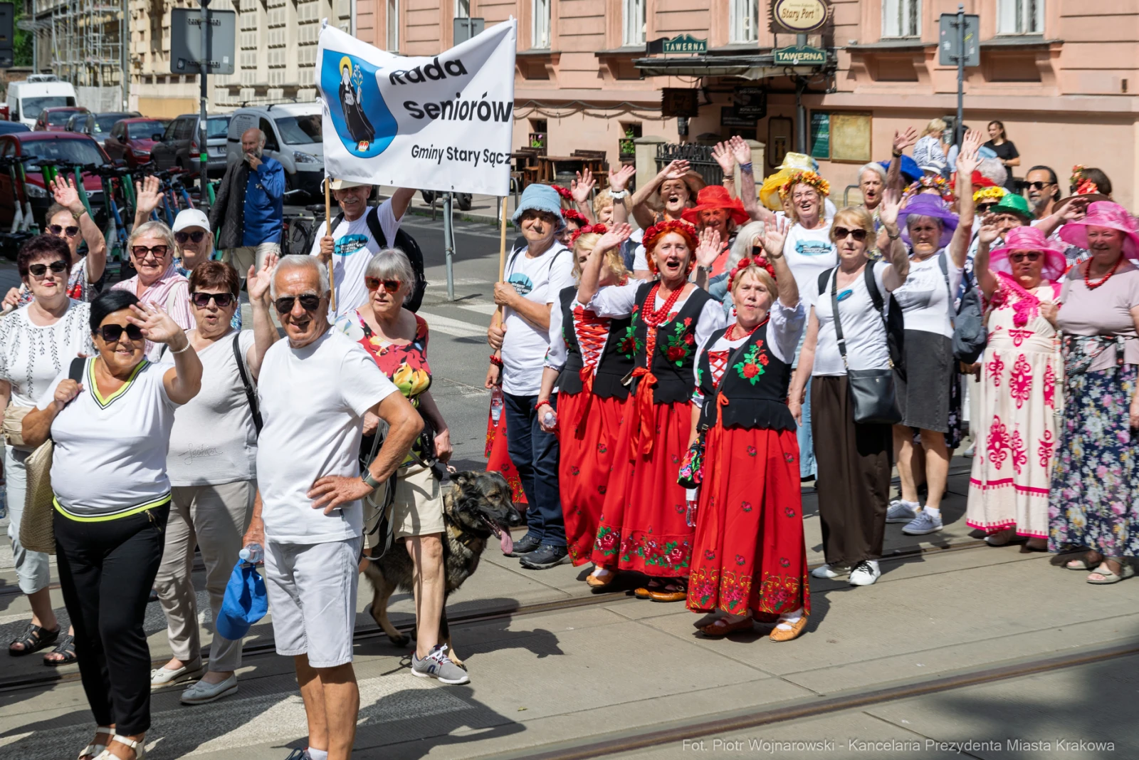 Grupa seniorów w kolorowych strojach, machająca flagą i pozująca do zdjęcia.  Autor: Piotr Wojnarowski