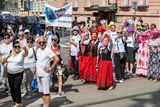 Grupa seniorów w kolorowych strojach, machająca flagą i pozująca do zdjęcia.
