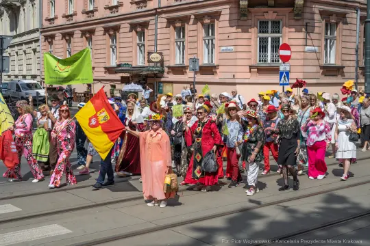 Tłum kolorowo ubranych ludzi z flagami i kwiatami na ulicy.