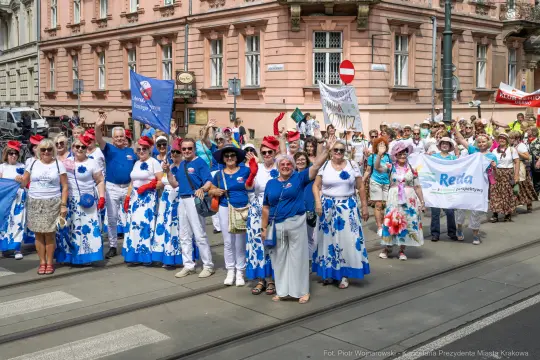 Grupa ludzi w kolorowych strojach podczas parady, trzymających transparenty i flagi.