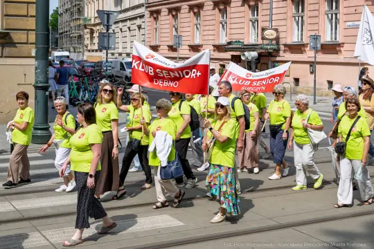 Grupa seniorów w zielonych koszulkach maszeruje z transparentami w mieście.