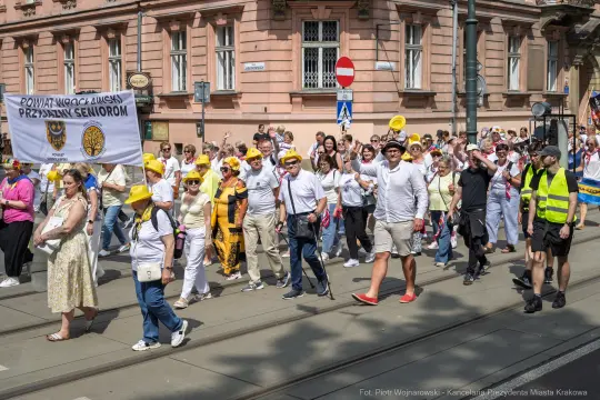 Marsz seniorów z transparentami i żółtymi nakryciami głowy na ulicach miasta.