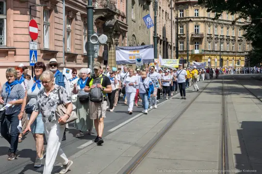 Grupa ludzi idąca ulicą, niosąca transparenty i flagi.