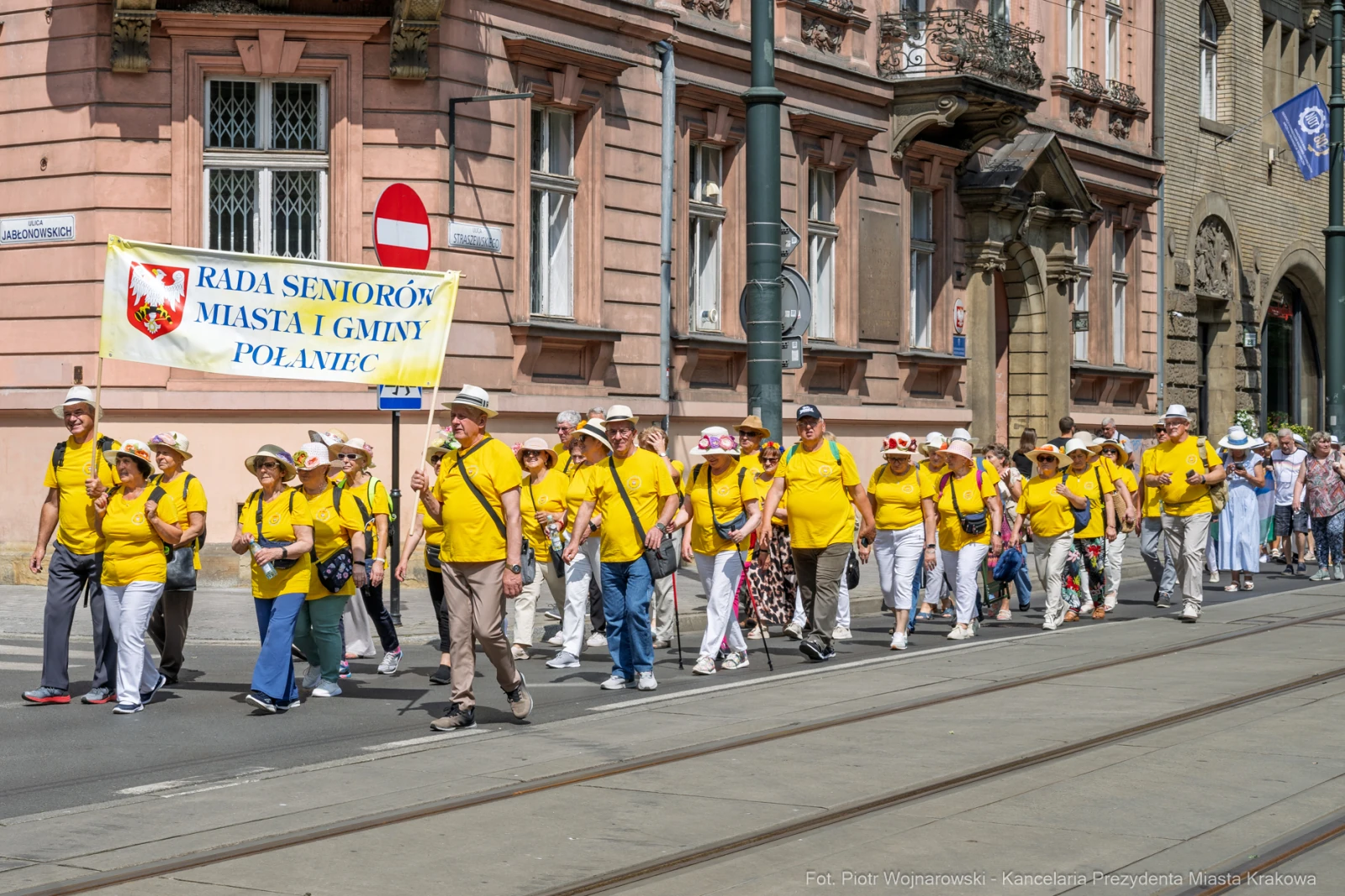 Grupa seniorów w żółtych koszulkach idzie ulicą z transparentem.  Autor: Piotr Wojnarowski