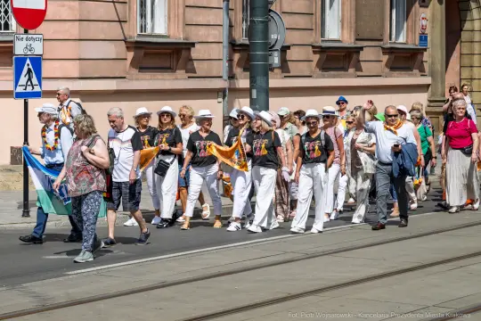 Grupa osób w białych ubraniach i kapeluszach idzie ulicą podczas wydarzenia.