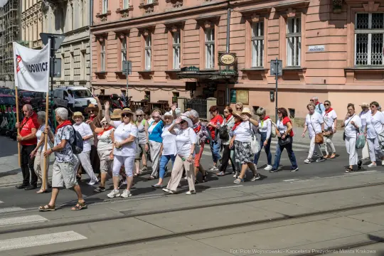 Grupa osób w białych koszulach i czerwonych chustach maszeruje ulicą.
