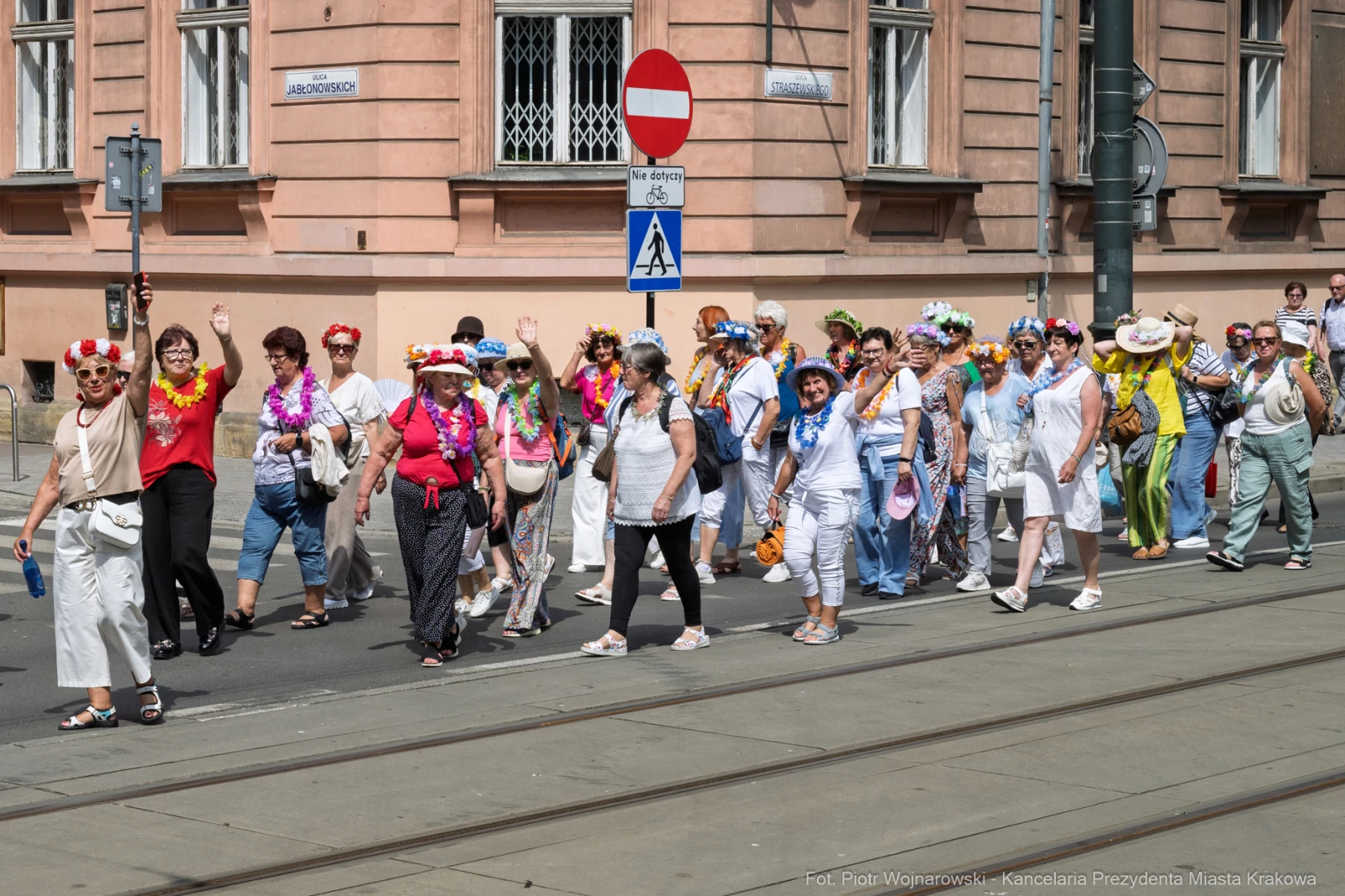 Grupa osób w kolorowych strojach i kwiatowych naszyjnikach maszeruje ulicą.  Autor: Piotr Wojnarowski