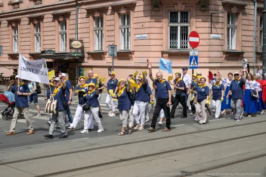 Grupa ludzi w koszulkach z logo, maszerująca ulicą podczas wydarzenia.