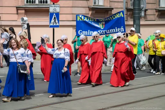 Grupa seniorów w kolorowych strojach idzie w parady z transparentem.