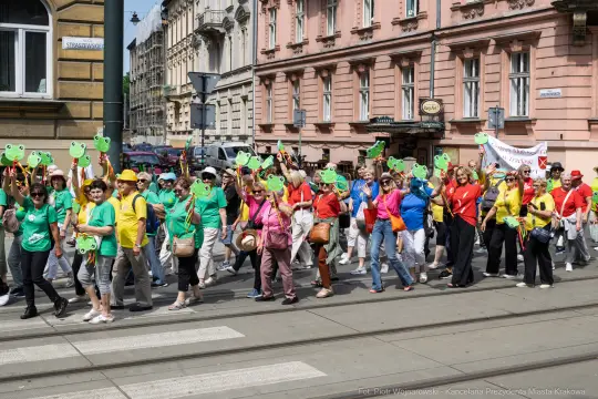 Grupa ludzi w kolorowych koszulkach trzymających zielone kartoniki podczas marszu.