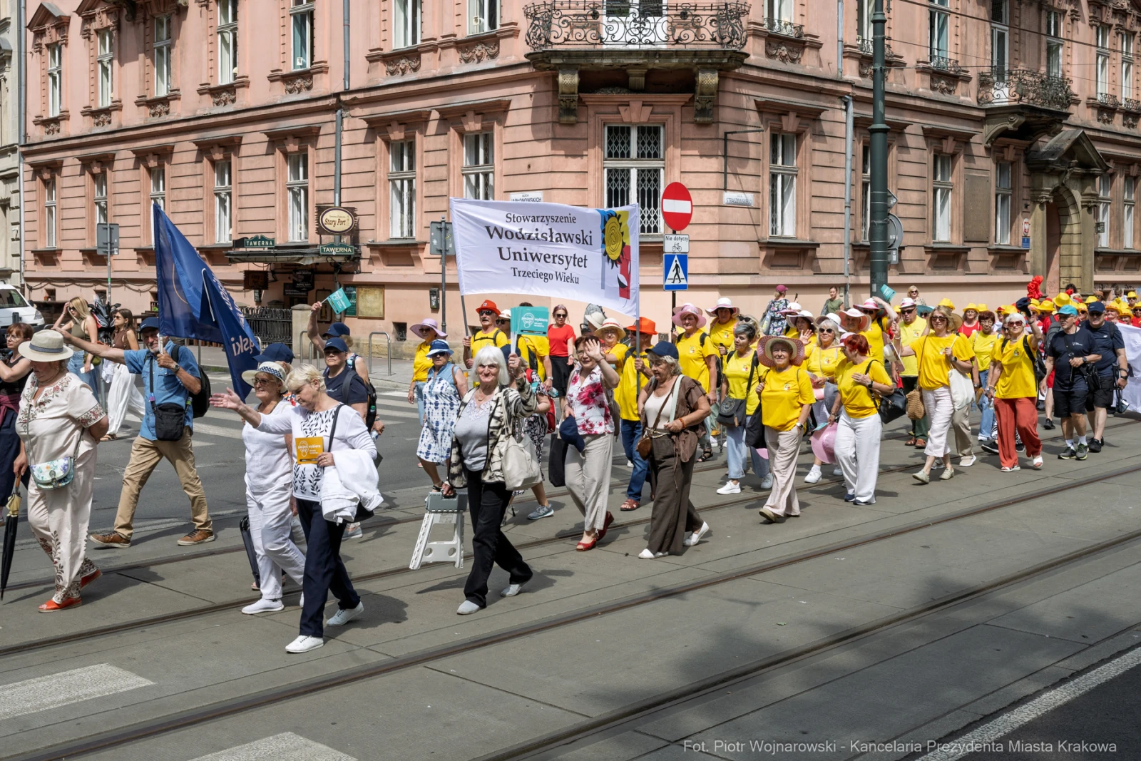 Grupa ludzi w żółtych koszulach maszerująca ulicą z transparentem Uniwersytetu Trzeciego Wieku.  Autor: Piotr Wojnarowski