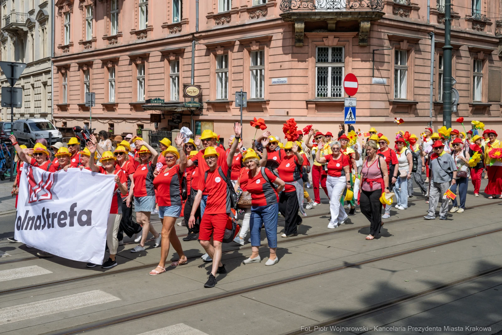 Grupa ludzi w czerwonych strojach i żółtych kapeluszach maszeruje z transparentem.  Autor: Piotr Wojnarowski