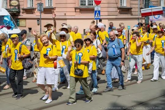 Grupa ludzi w żółtych koszulkach maszeruje podczas wydarzenia, trzymając transparenty i uśmiechając się.
