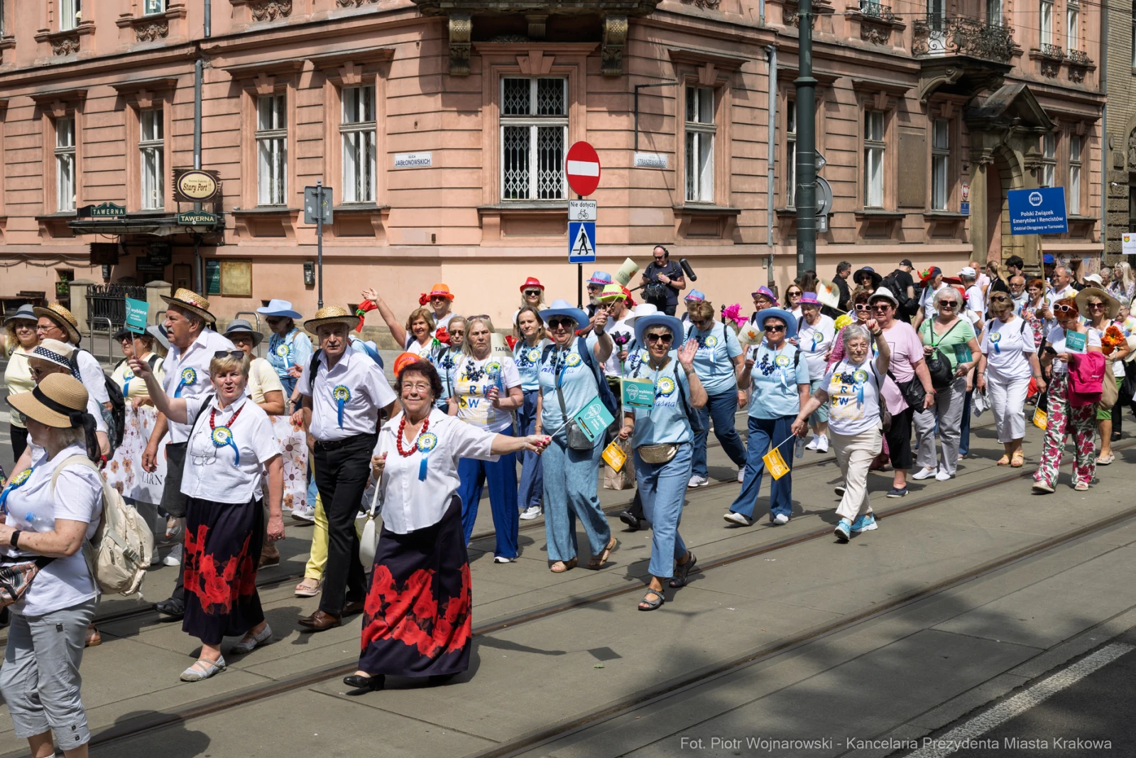 Grupa ludzi w kolorowych strojach maszeruje ulicą, niektórzy machają rękami.  Autor: Piotr Wojnarowski