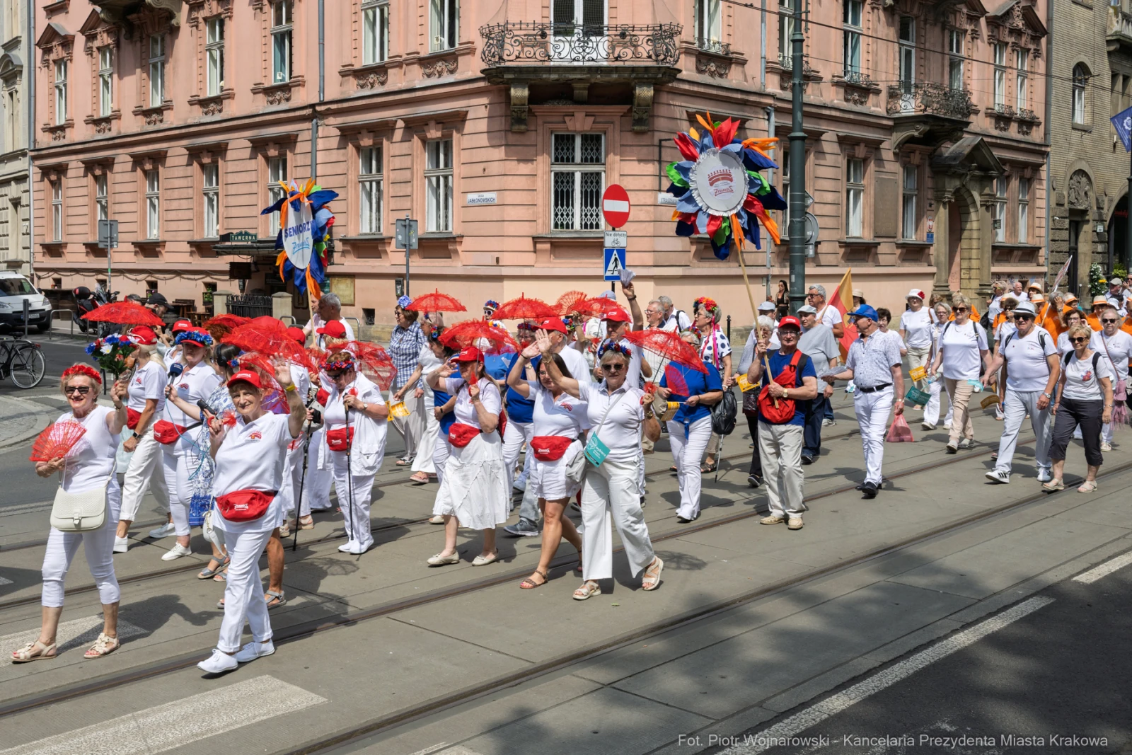 Grupa ludzi w białych strojach z parasolkami i kolorowymi akcesoriami podczas parady.  Autor: Piotr Wojnarowski