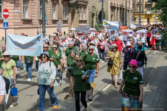 Marsz seniorów w Krakowie, uczestnicy niosą transparenty i flagi.