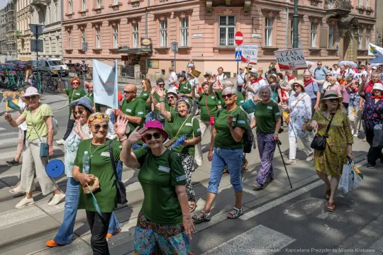 Grupa osób w zielonych koszulkach maszeruje ulicą, machając rękami i trzymając transparenty.