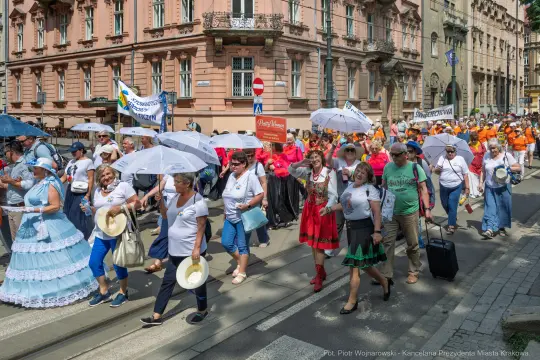 Grupa ludzi w różnorodnych strojach, niosących parasole, uczestniczy w parady ulicznej.