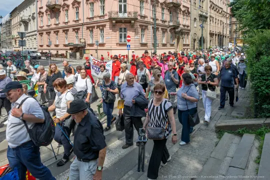 Tłum ludzi idący ulicą, część z transparentami, w różnorodnych strojach.