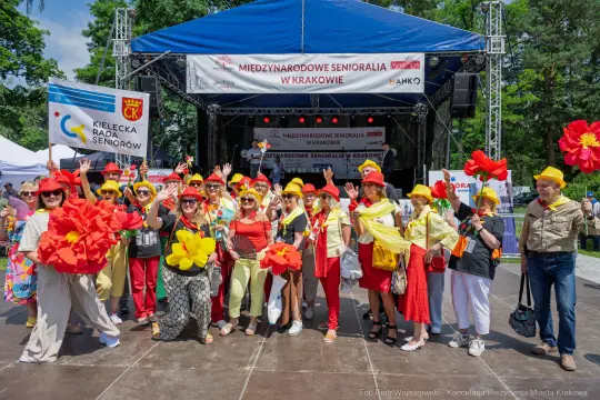 Grupa seniorów w kolorowych strojach z kwiatami na festiwalu w Krakowie.