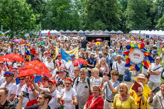 Tłum ludzi na festiwalu, kolorowe parasole, flagi i radosna atmosfera.