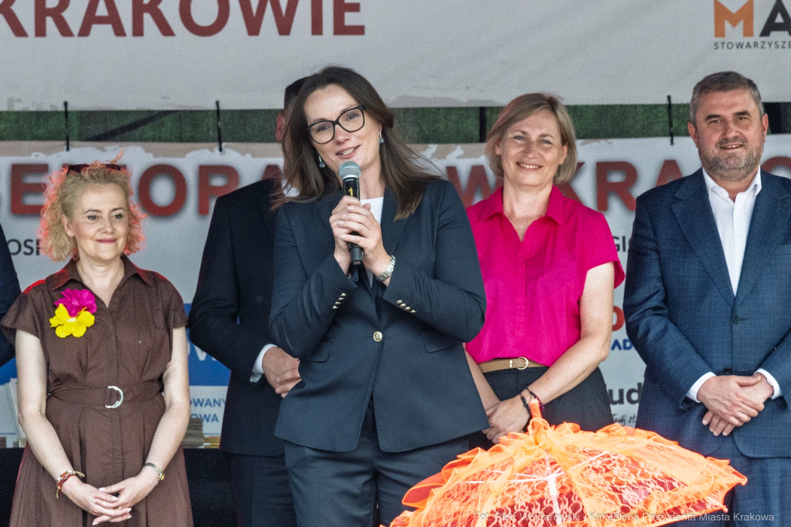 Kobieta w garniturze przemawia na tle grupy osób podczas wydarzenia w Krakowie.  Autor: Piotr Wojnarowski