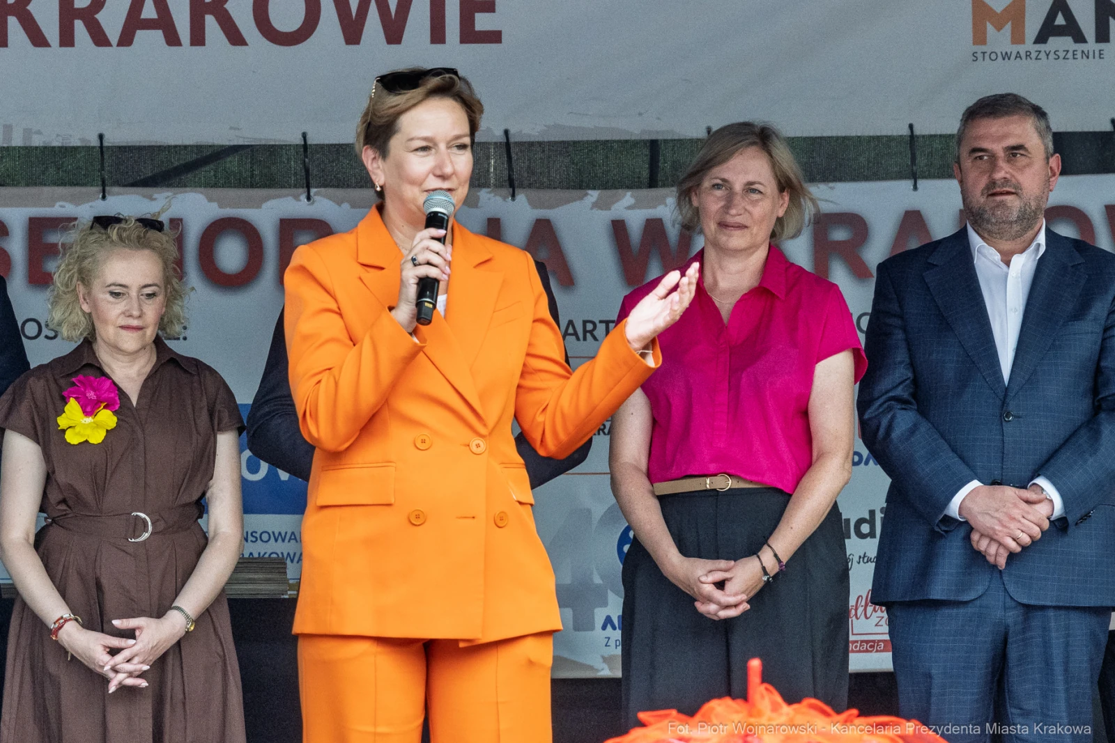 Kobieta w pomarańczowym garniturze przemawia do zgromadzonego tłumu, obok niej stoją inne osoby.  Autor: Piotr Wojnarowski