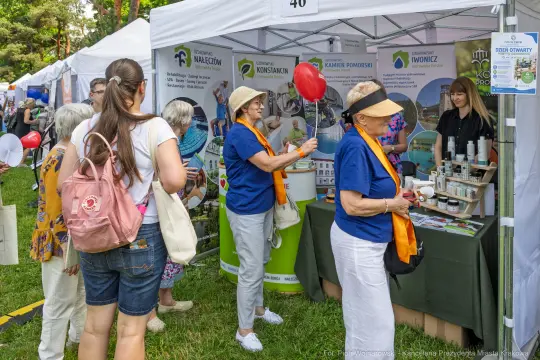 Kobiety z balonami przy stoisku informacyjnym, uczestnicy wydarzenia plenerowego.