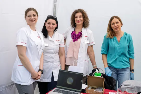 Cztery kobiety w białych fartuchach, przy stole z laptopem i akcesoriami medycznymi.