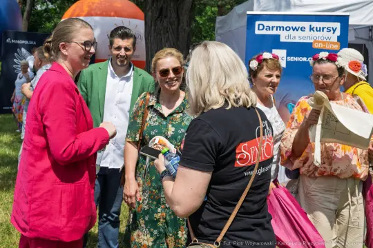 Grupa osób w różnorodnych strojach, rozmawiających i uśmiechających się podczas wydarzenia.