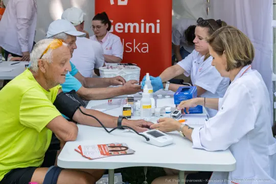 Mężczyzna w trakcie badania ciśnienia krwi przez pielęgniarkę. W tle stoiska medyczne.