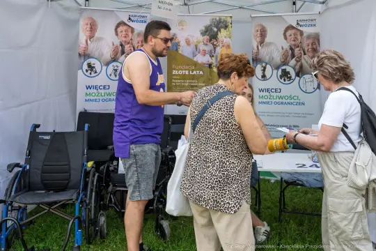 Ludzie w namiocie informacyjnym, rozmawiający o fundacji wspierającej osoby starsze.