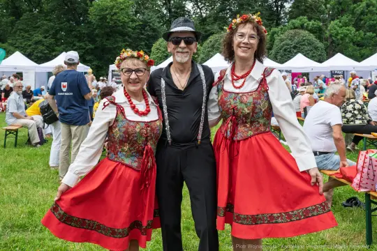 Trzy osoby w tradycyjnych strojach ludowych, w otoczeniu festiwalu.