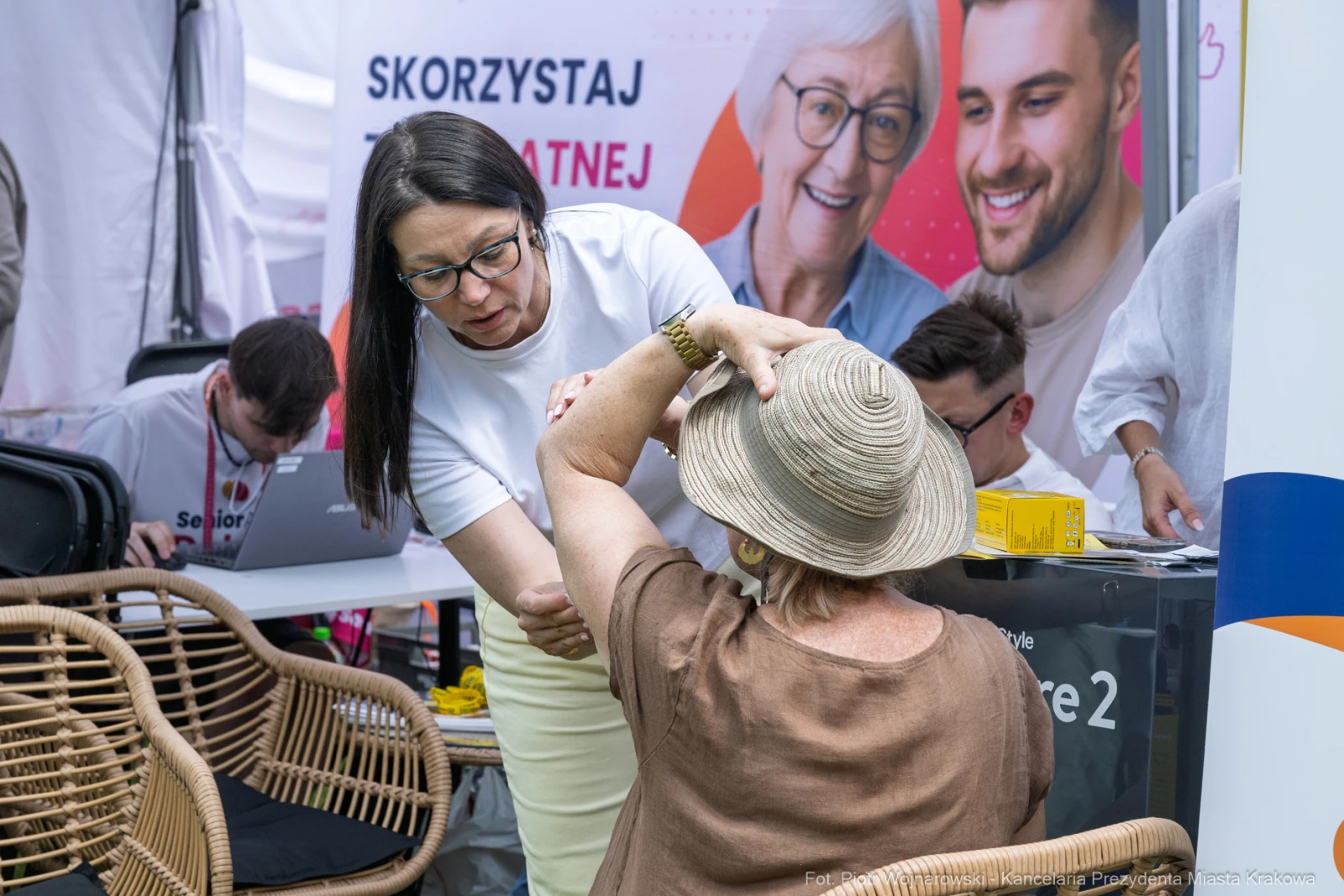 Kobieta w białej koszulce pomaga starszej pani w kapeluszu podczas wydarzenia.  Autor: Piotr Wojnarowski