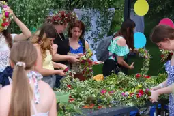 Kobiety i dziewczęta tworzą wianki z kwiatów i zieleni.