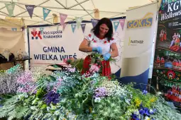 Kobieta w stroju ludowym układa kwiaty na stoisku.