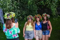 Cztery kobiety w kwiecistych wiankach pozują do zdjęcia w plenerze.