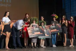 Kobiety na scenie odbierają nagrody, w tle dekoracje i aplauz publiczności.
