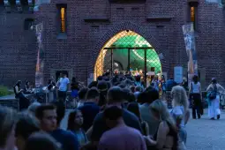 Tłum ludzi czekających przed wejściem do budynku z dużymi oknami.