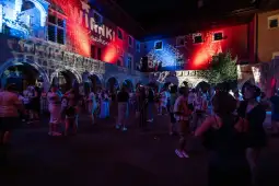 Impreza w plenerze z tańcem, kolorowe światła i tłum ludzi w historycznym otoczeniu.