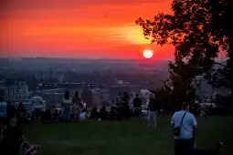 Zachód słońca nad miastem, ludzie siedzący na trawie.