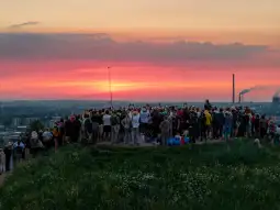 Tłum ludzi na wzgórzu podziwiający zachód słońca.