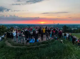 Grupa ludzi obserwujących zachód słońca z wzgórza.
