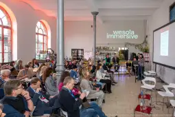 Konferencja z uczestnikami w sali, prezentacja na ekranie, atmosfera networkingowa.