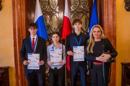 Czwórka młodych ludzi trzyma dyplomy, stojąc przed flagami Polski i Rosji.