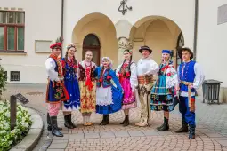Grupa osób w tradycyjnych polskich strojach ludowych, pozująca w malowniczej scenerii.
