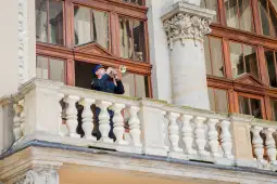 Mężczyzna w mundurze gra na trąbce z balkonu.