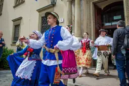 Grupa osób w tradycyjnych strojach ludowych tańczących na ulicy.