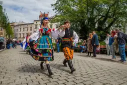 Para w tradycyjnych strojach ludowych tańczy na ulicy, otoczona przez tłum widzów.